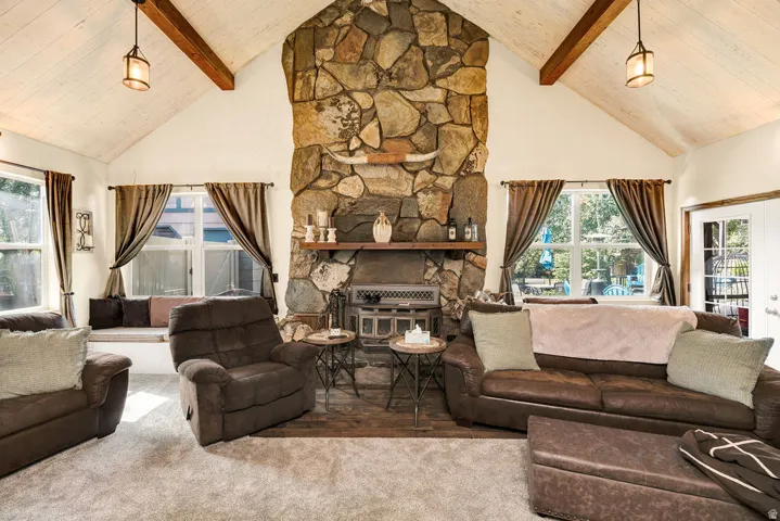 Living area featuring a floor-to-ceiling stone fireplace, vaulted ceiling with exposed wood beams, and a built-in window seat
