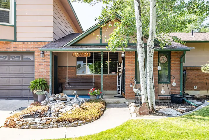 Brick and siding exterior with an attached garage, covered front porch, and a landscaped front yard with mature trees