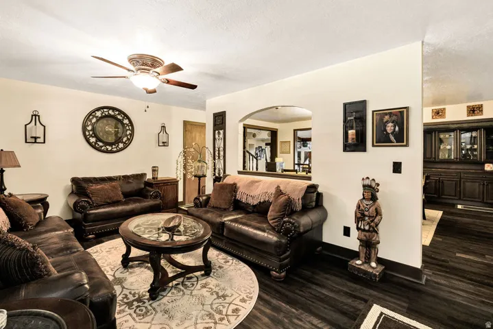 Spacious living area featuring dark wood-finish flooring, a ceiling fan with integrated lighting, and an arched entryway