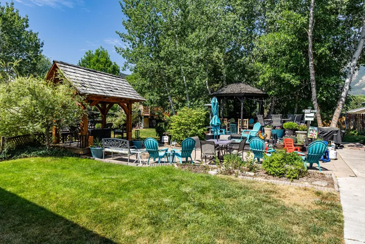 Expansive backyard featuring a manicured lawn, a wooden gazebo with a shingled roof, a paved patio area, mature trees, and a second dark-roofed gazebo