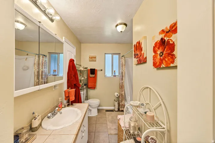 Bathroom featuring a white vanity with an integrated sink, a large mirrored medicine cabinet with overhead lighting, and tile flooring