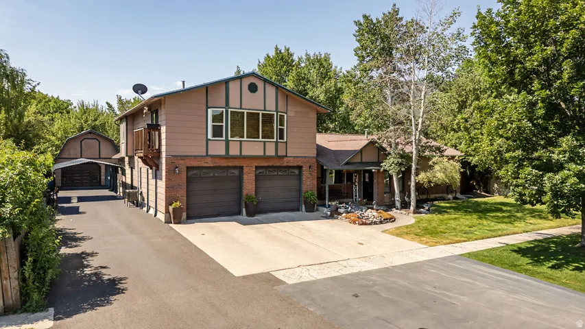 Expansive property featuring a two-car garage, an additional detached garage with an attached carport, a paved driveway, and mature landscaping
