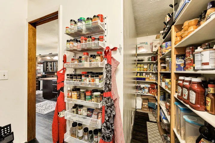 Dedicated pantry space featuring extensive built-in shelving, organized storage solutions, wood-finish flooring, and a visible doorway to an adjacent room