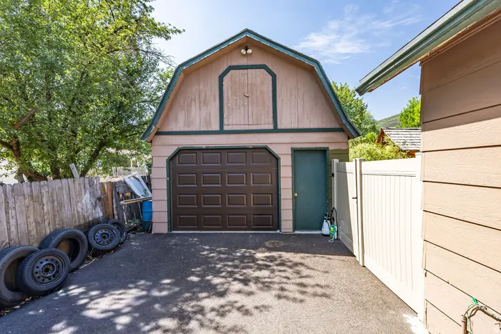 Two-story detached garage with a gambrel roofline, featuring a paneled roll-up garage door and a side entry door