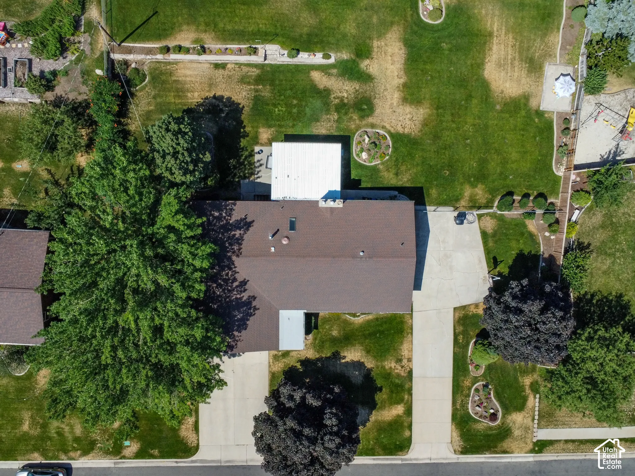 Expansive lot featuring a large residential structure with a brown shingle roof, two distinct concrete driveways, mature trees, and a substantial green lawn area