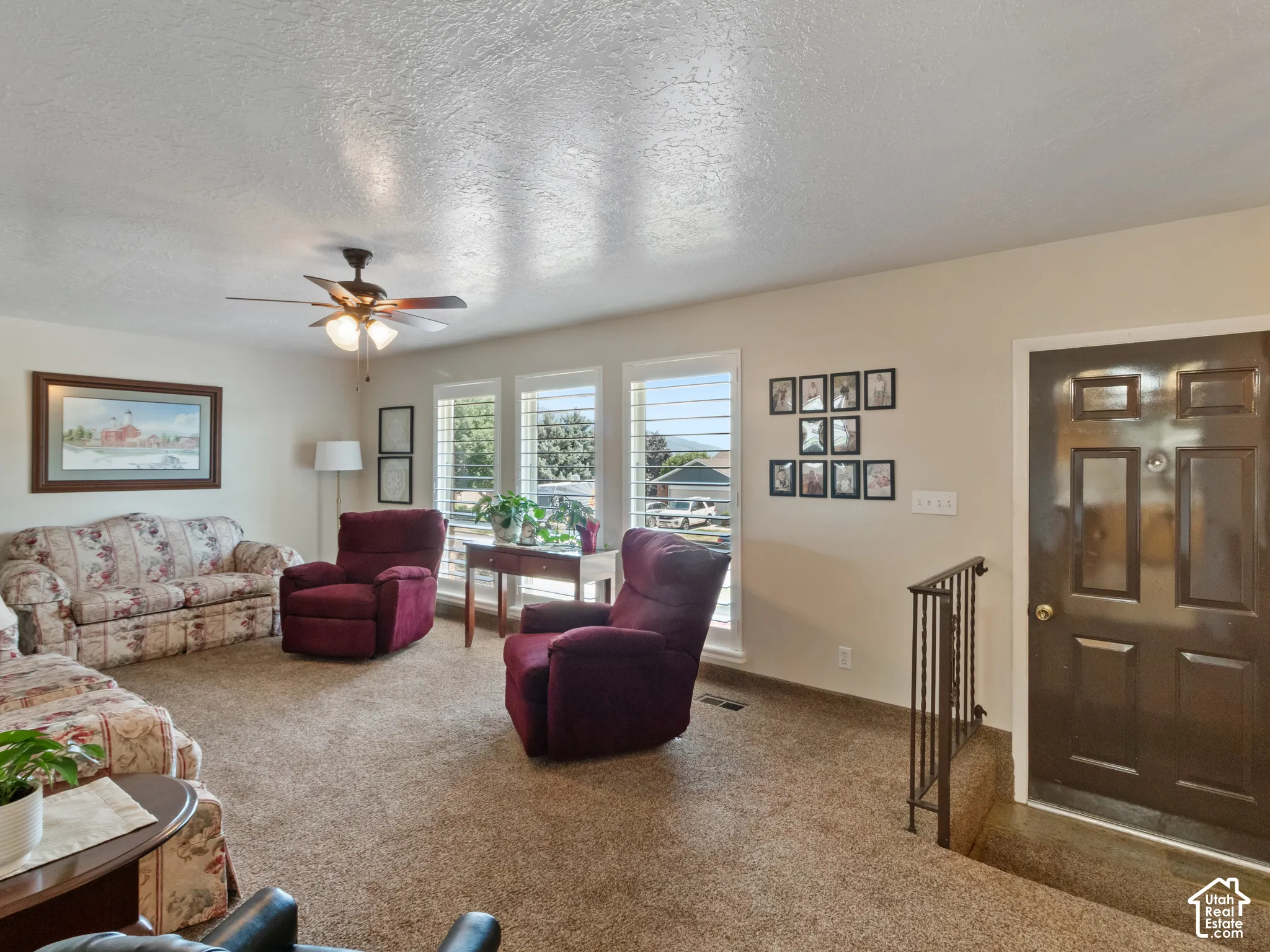 Living room featuring multiple windows with plantation shutters, a ceiling fan, and brown carpet flooring