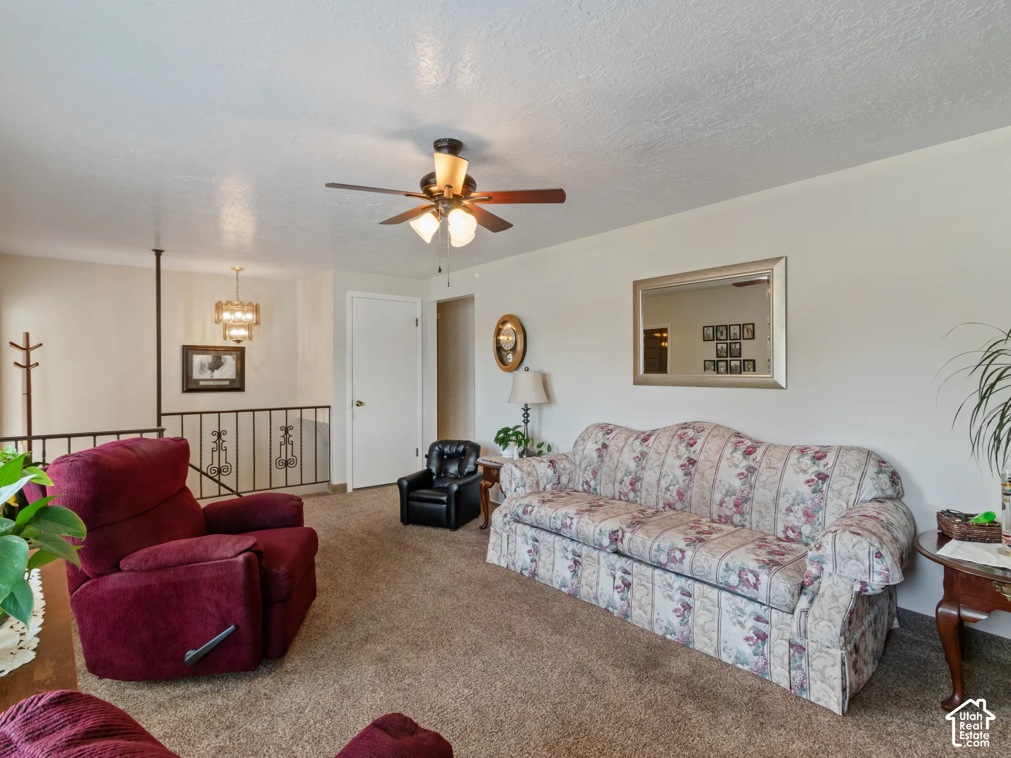 Carpeted living area featuring a ceiling fan with light fixture, white walls, and a staircase with a black metal railing