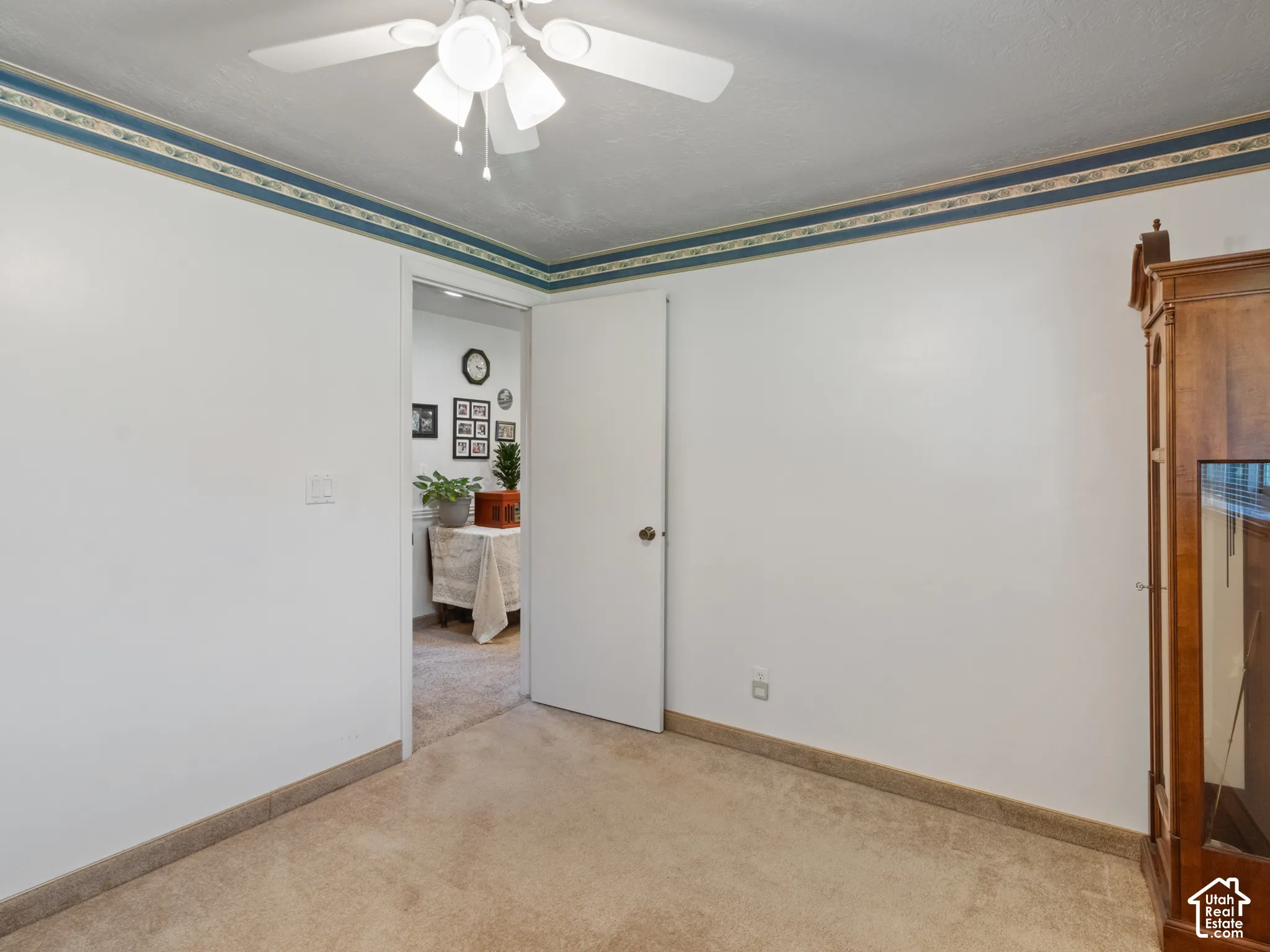 Carpeted room featuring white walls with a decorative border, a ceiling fan, and a light-colored door