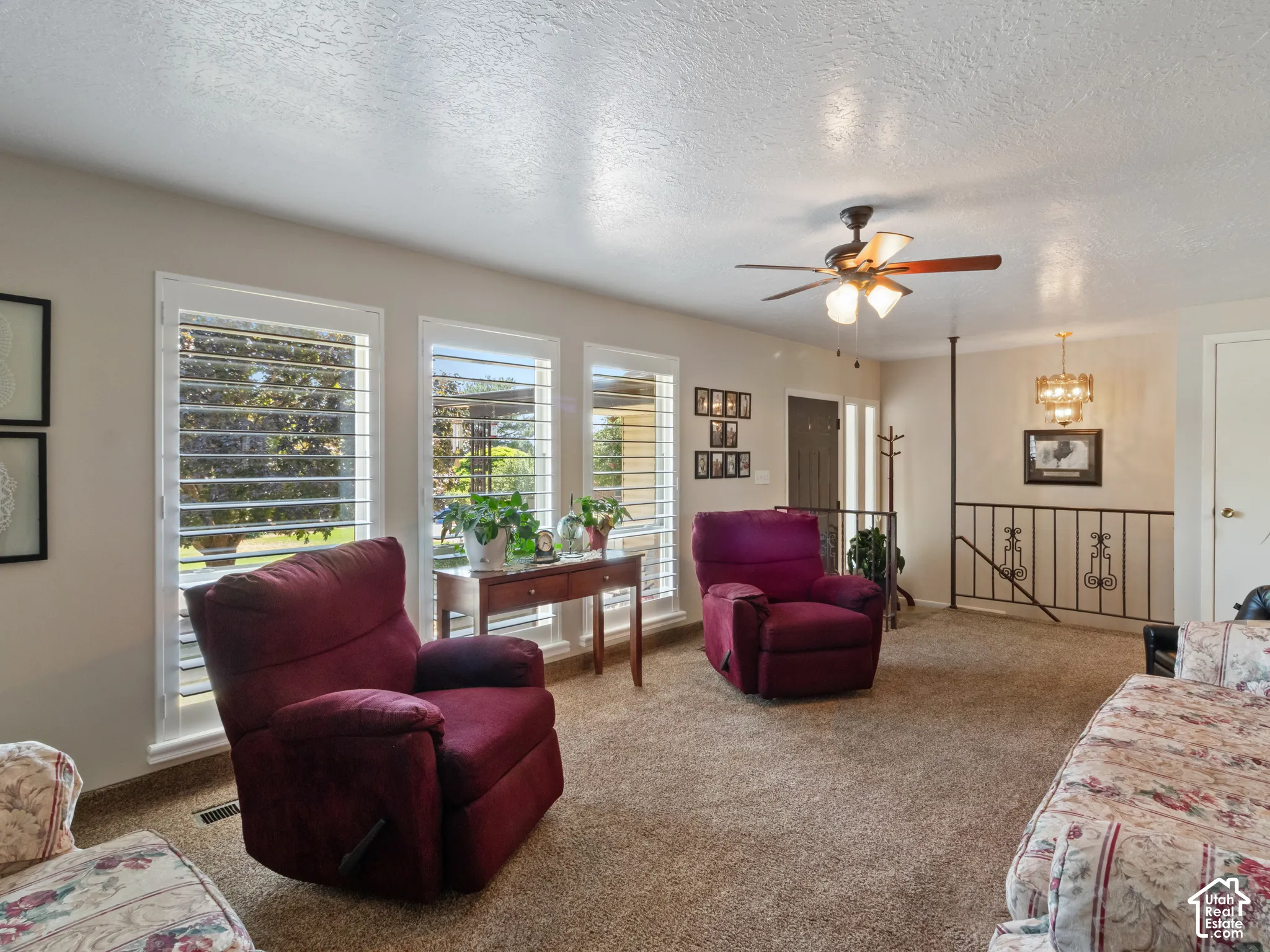 Living area featuring multiple windows with plantation shutters, a ceiling fan, and carpeted flooring