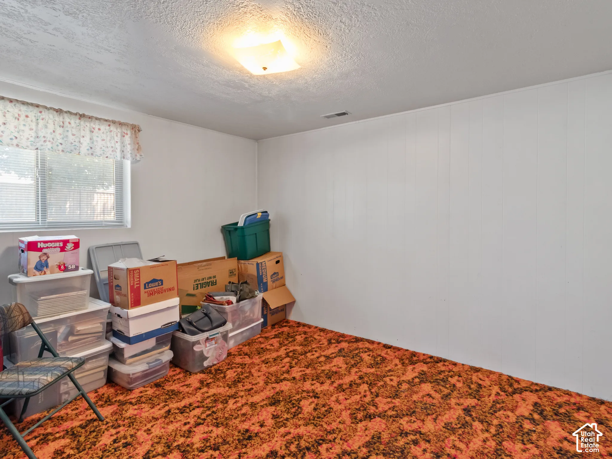 Room featuring orange and black patterned carpet, white paneled walls, and a window with blinds