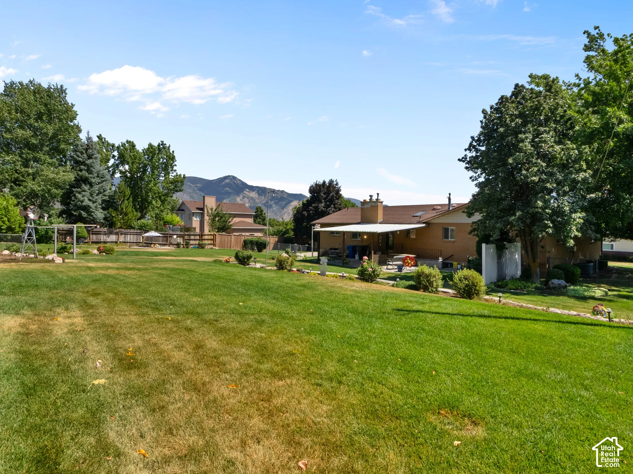 Expansive backyard featuring a large green lawn, mature trees, and a covered patio area