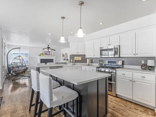 Kitchen featuring white cabinetry, stainless steel appliances, a dark-toned island with a light countertop, a gray tile backsplash, and wood-finish flooring