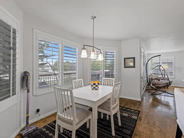 Dining area featuring multiple windows with plantation shutters, wood-finish flooring, a modern chandelier with frosted glass shades, and light gray wall paint