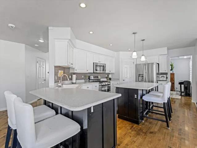 Contemporary kitchen featuring white cabinetry, stainless steel appliances, dual islands with quartz countertops, wood-finish flooring, and recessed lighting
