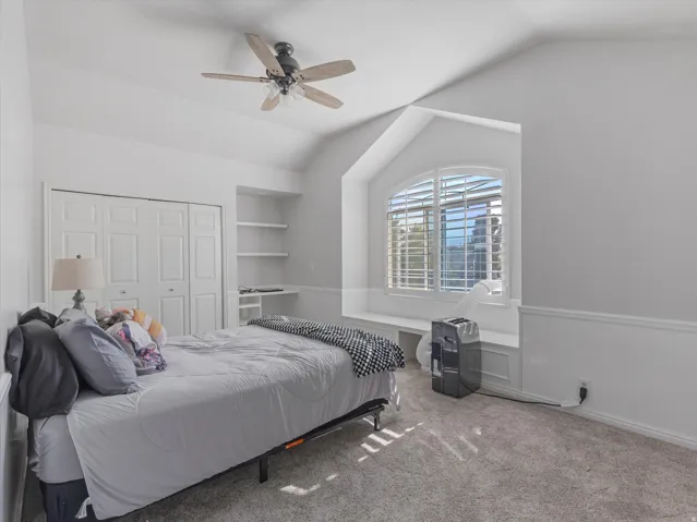 Room featuring a vaulted ceiling with a ceiling fan, a large arched window with plantation shutters, built-in shelving, a window bench, and wainscoting