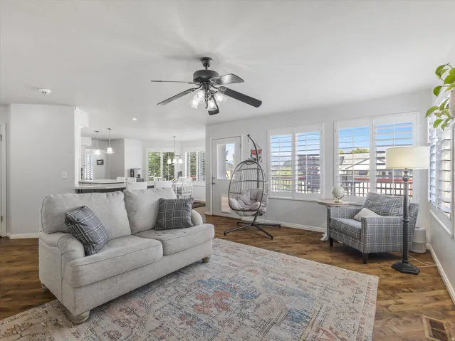 Open-concept living space featuring wood-finish flooring, white walls, and a ceiling fan with integrated lighting
