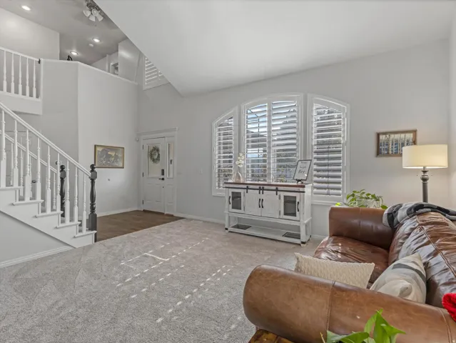 Vaulted ceiling entry featuring a two-story staircase with white balusters, wood-finish flooring, and arched windows with plantation shutters