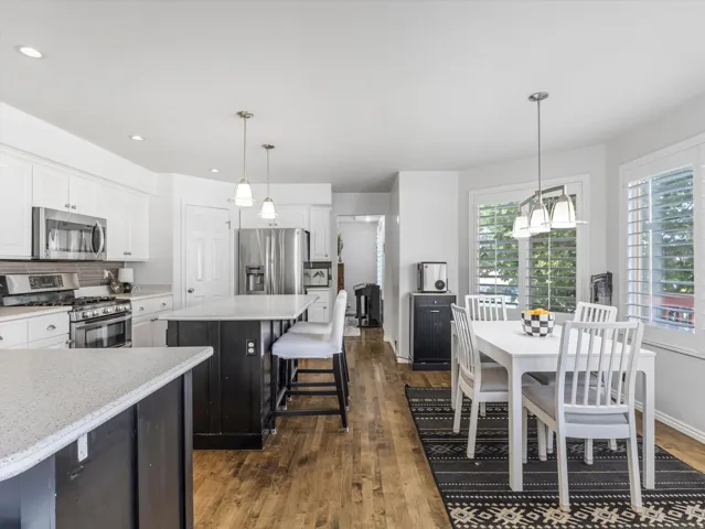Open-concept kitchen and dining area featuring a dark wood island with light countertops, stainless steel appliances, white cabinetry, and wood-finish flooring