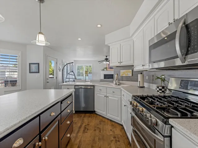 Kitchen featuring an expansive island with a light-toned countertop, white cabinetry with crown molding, stainless steel appliances, a gas range, and wood-finish flooring