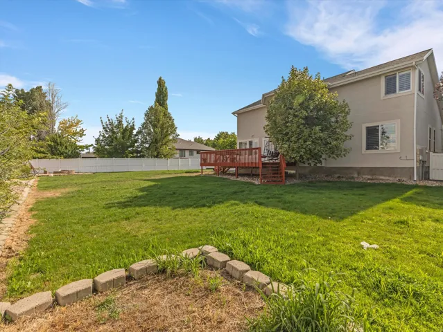 Expansive green space featuring a multi-level wood deck, white privacy fencing, and a stone-lined garden area