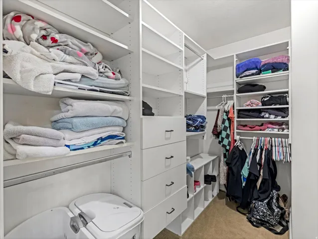 Custom closet system featuring white shelving, multiple hanging rods, built-in drawers with dark hardware, and integrated storage cubbies