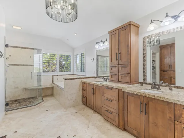 Spacious bathroom featuring a dual vanity with granite countertops, a built-in soaking tub, and a glass-enclosed shower with a tiled bench