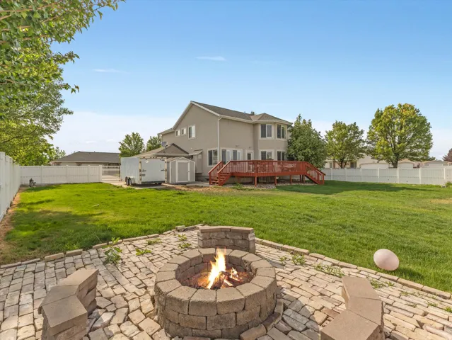 Expansive backyard featuring a stone paver patio with built-in fire pit, a large wooden deck, and a green lawn