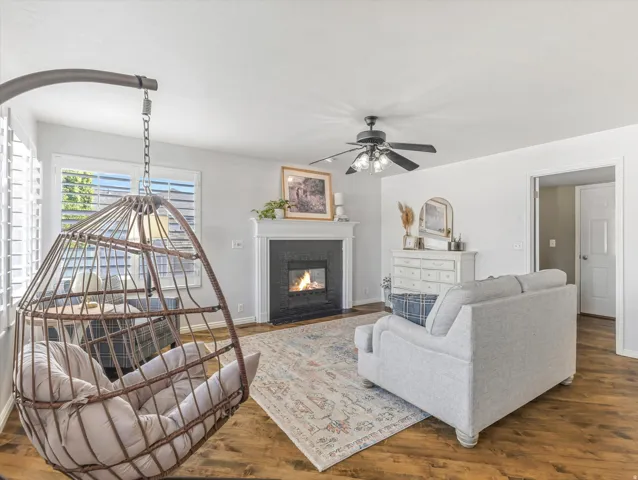 Living space featuring wood-finish flooring, a fireplace with a white mantel, and a ceiling fan with integrated lighting