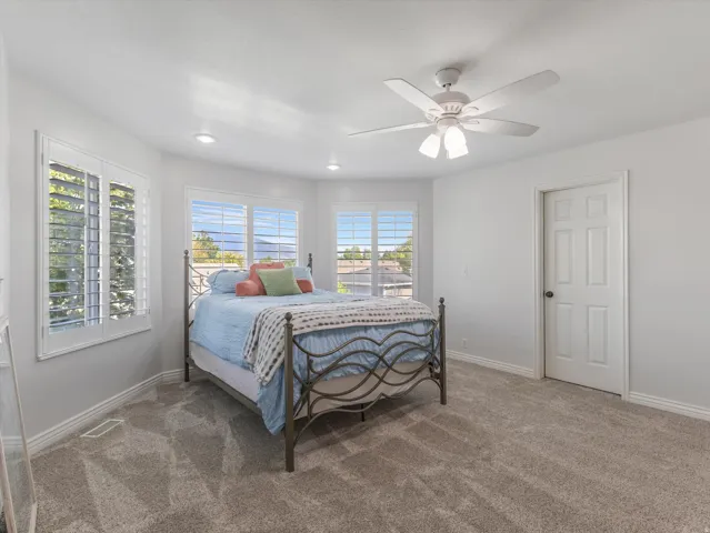 Bright bedroom featuring multiple windows with louvered shutters, recessed lighting, a ceiling fan with integrated lighting, and neutral carpet flooring