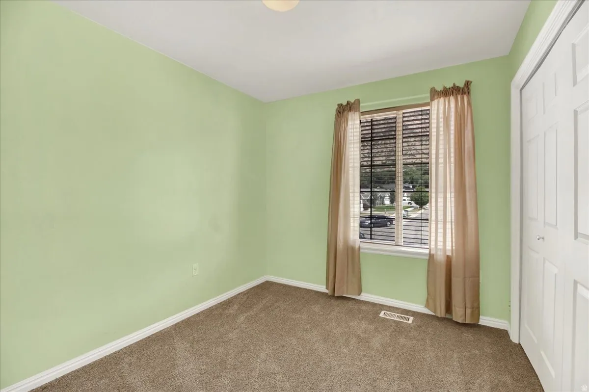 Bright room featuring a double-paned window with horizontal blinds, light green walls, a white baseboard, and brown carpet flooring