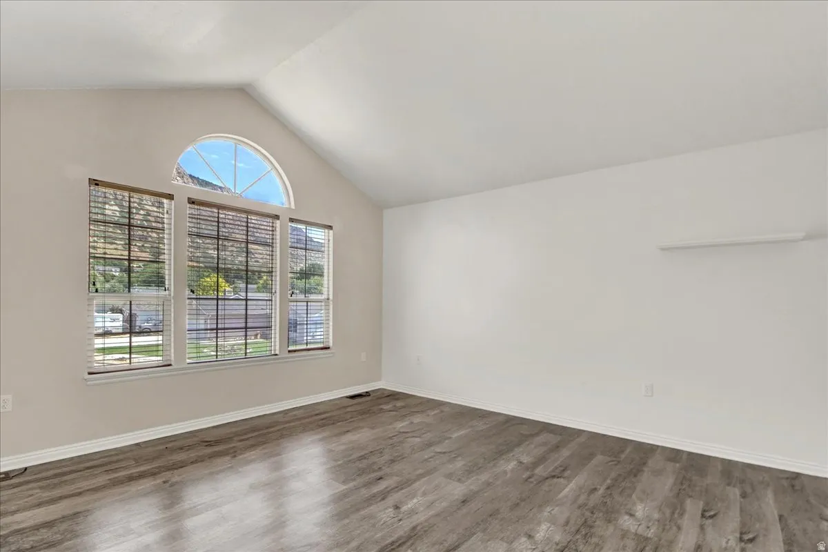 Spacious room featuring vaulted ceilings, wood-finish flooring, a large window array, and an arched transom window