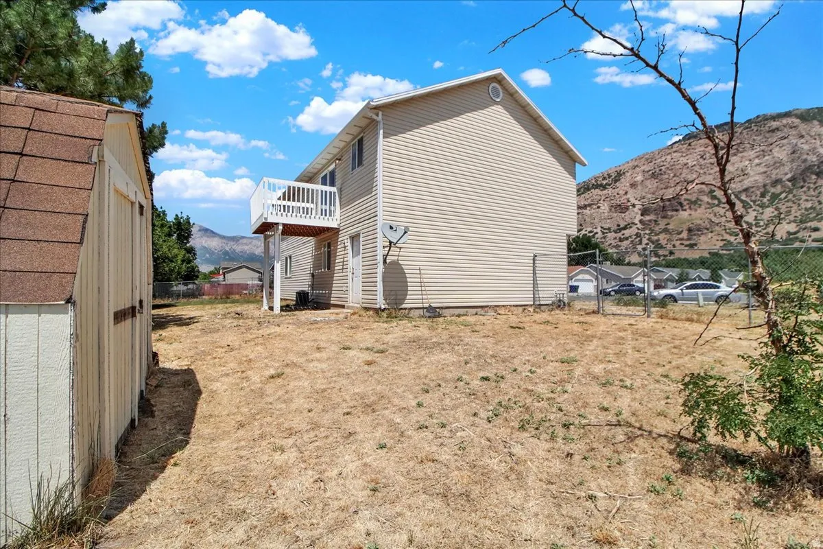 Rear exterior back yard featuring a two-story residence with beige siding, a second-story deck with white railing, and a ground-level door