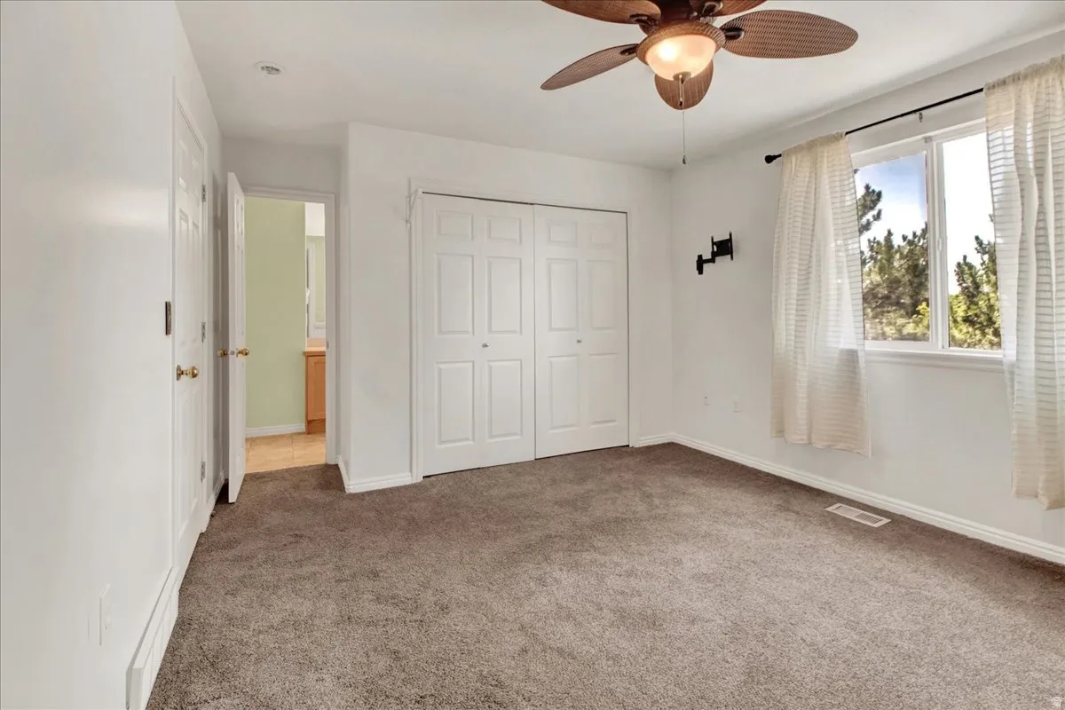 Primary bedroom carpeted interior space featuring a ceiling fan with integrated lighting, a double-door closet, and a white-framed window