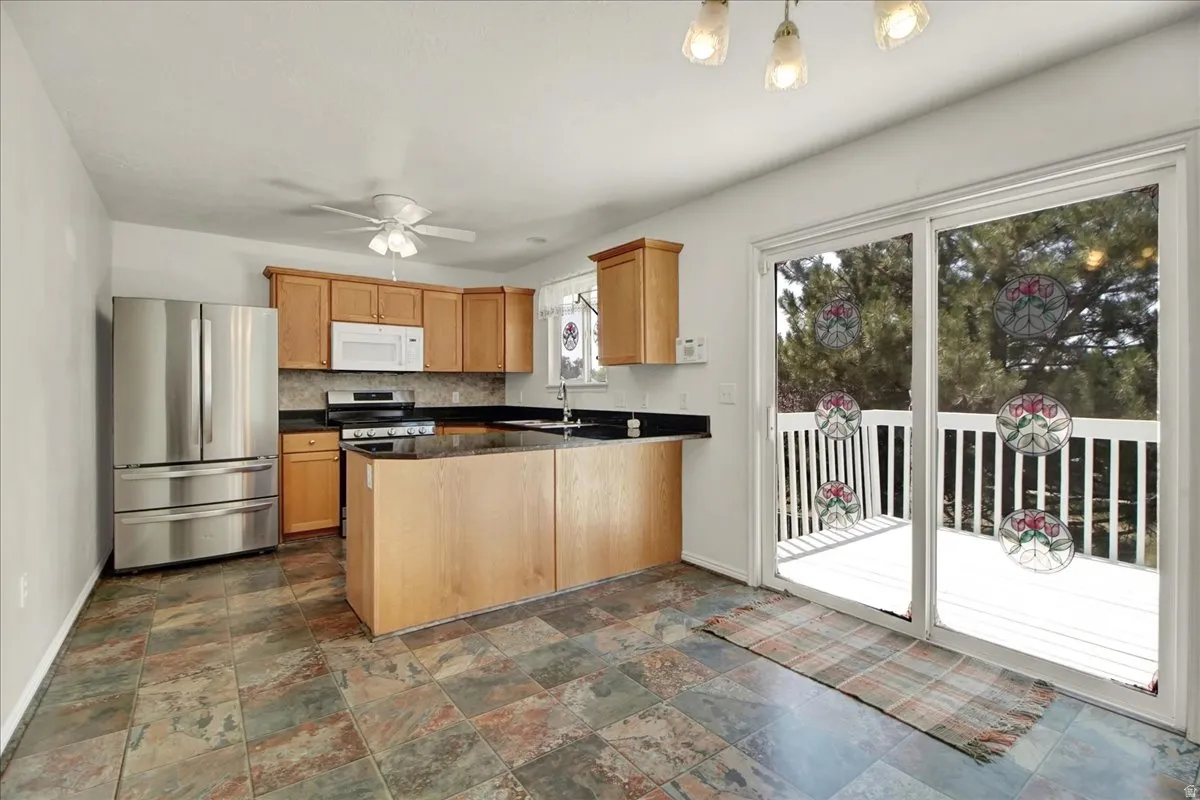 Kitchen featuring wood cabinetry, black countertops, stainless steel appliances, and slate-style floor tiling
