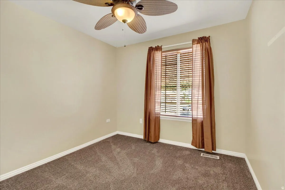 Neutral-toned room featuring a window with blinds and brown drapes, a ceiling fan with integrated lighting, and plush brown carpeting