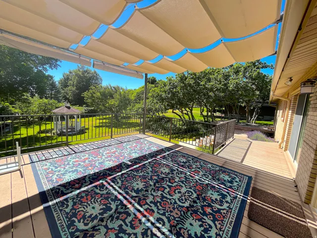 Spacious outdoor deck featuring a retractable fabric canopy, metal railings, and a wood-finish surface