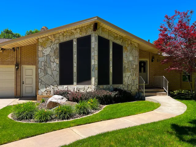 Exterior featuring a prominent stone facade, brick siding, a curved concrete pathway, a decorative rock garden, and a striking red-leafed tree