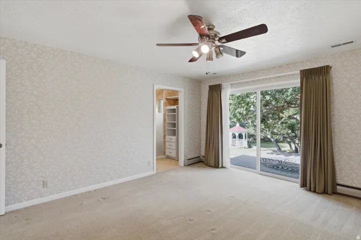 Room featuring a sliding glass door, patterned wallpaper, ceiling fan, and carpeted flooring