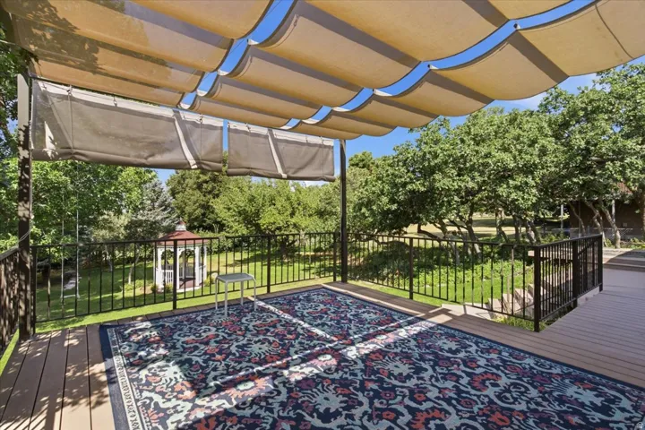 Expansive outdoor deck featuring wood-finish flooring, a retractable fabric canopy, and dark metal railings