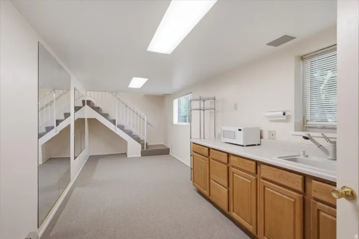 Lower level recreation space featuring a built-in wet bar with a single basin sink and wood-finish cabinetry