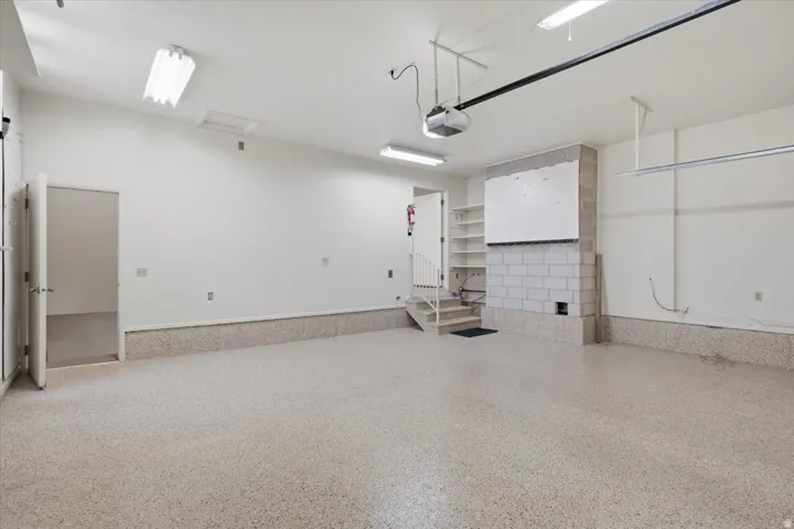 Spacious garage featuring a speckled epoxy floor, white painted walls, exposed block construction, built-in shelving, and a visible garage door opener mechanism