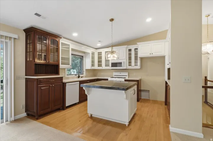 Open-concept kitchen featuring wood-finish flooring, a central island with a contrasting countertop, white upper cabinetry, and dark wood lower cabinetry