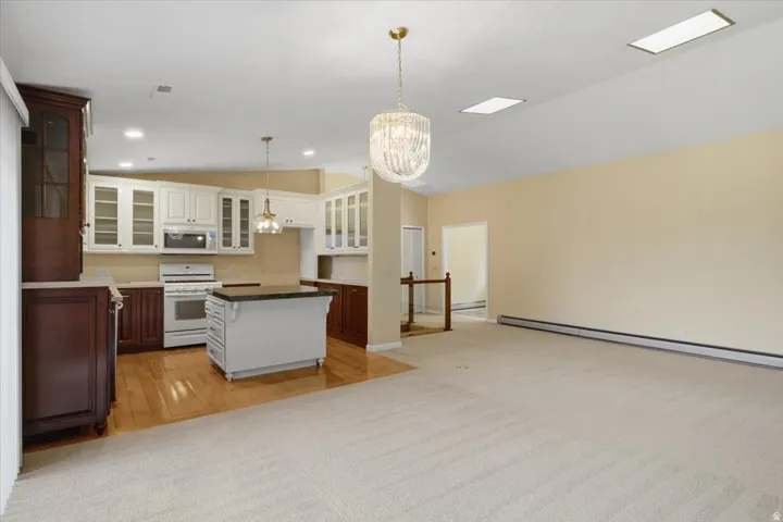 Open-concept living area featuring a kitchen with white and dark wood-finish cabinetry, a central island with a dark countertop, and a white range