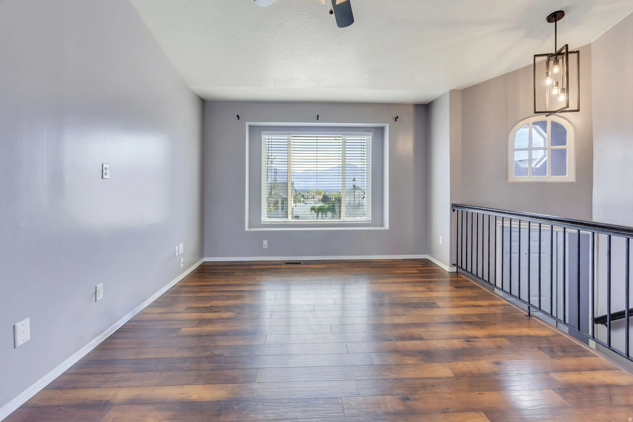 Spacious room featuring wood-finish flooring, a large window with blinds, and a distinctive arched window