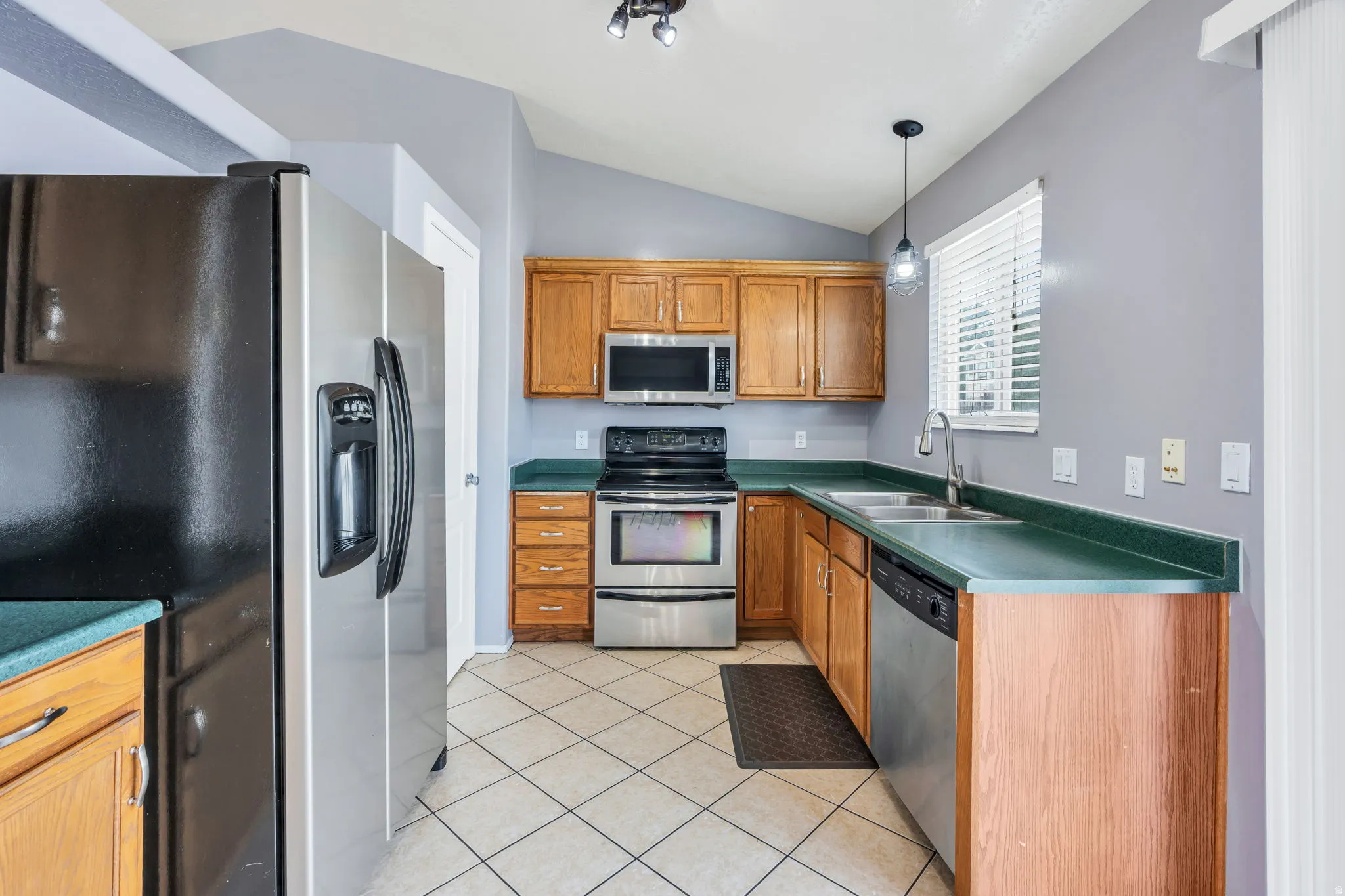 Kitchen featuring wood cabinetry, green countertops, stainless steel appliances, and diagonal tile flooring