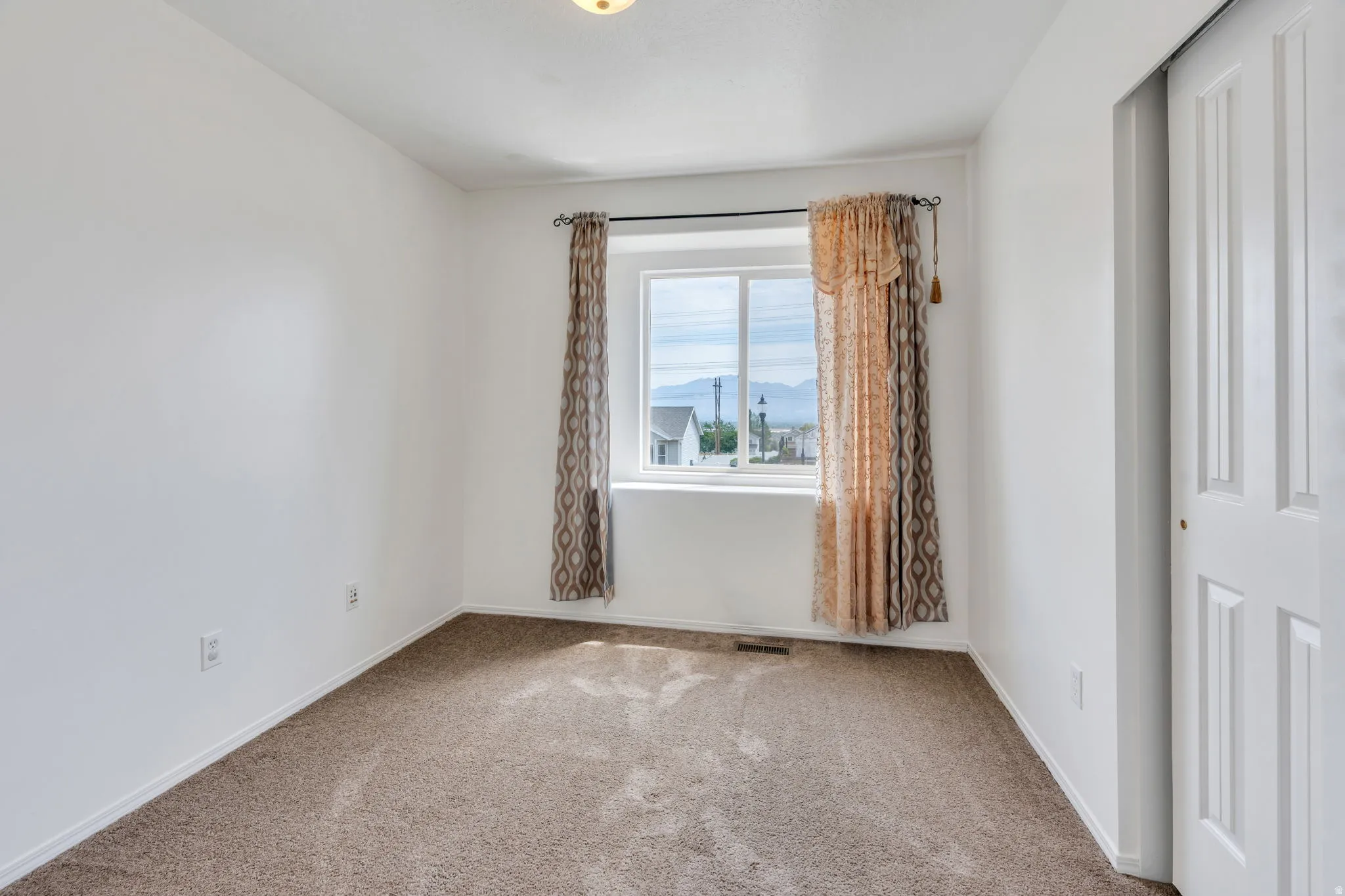 Bright room featuring a window with a mountain backdrop, neutral carpeting, white walls, and a bi-fold closet door