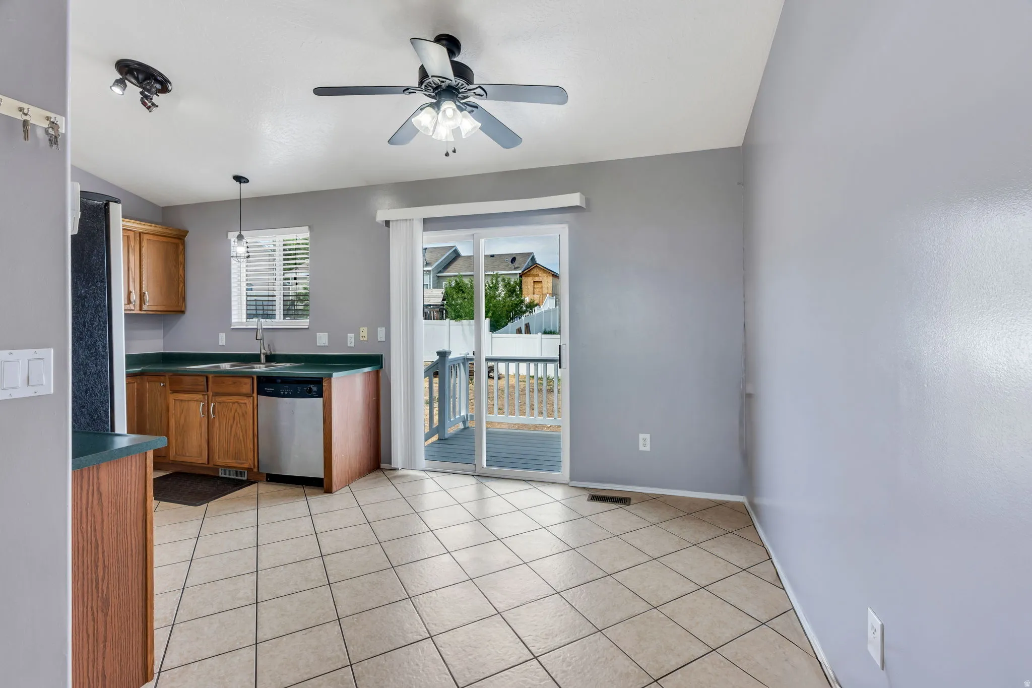 Kitchen area featuring tiled flooring, wood cabinetry, green countertops, and a stainless steel dishwasher