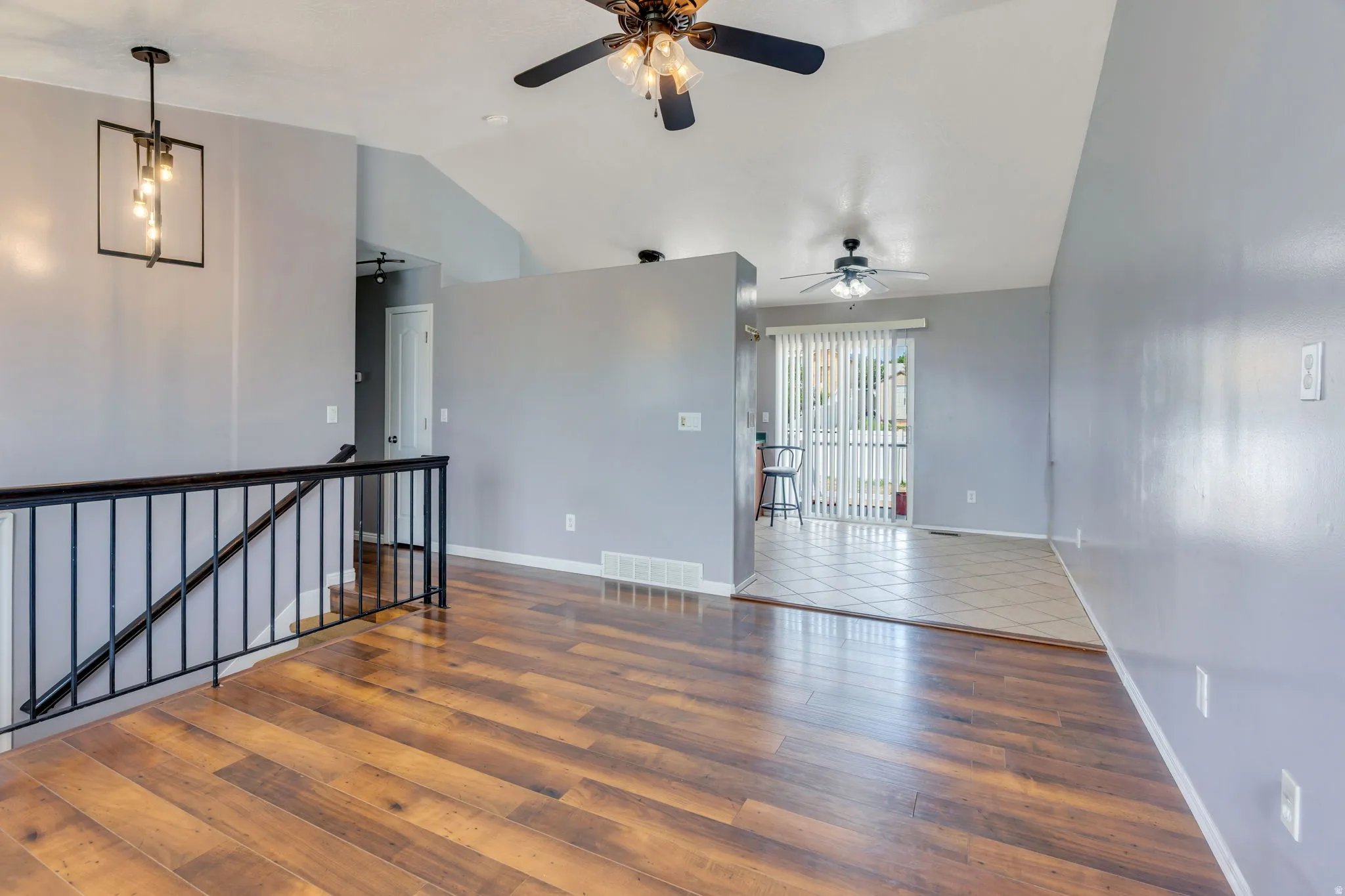 Spacious room featuring wood-finish flooring, light gray walls, and a contemporary black metal chandelier