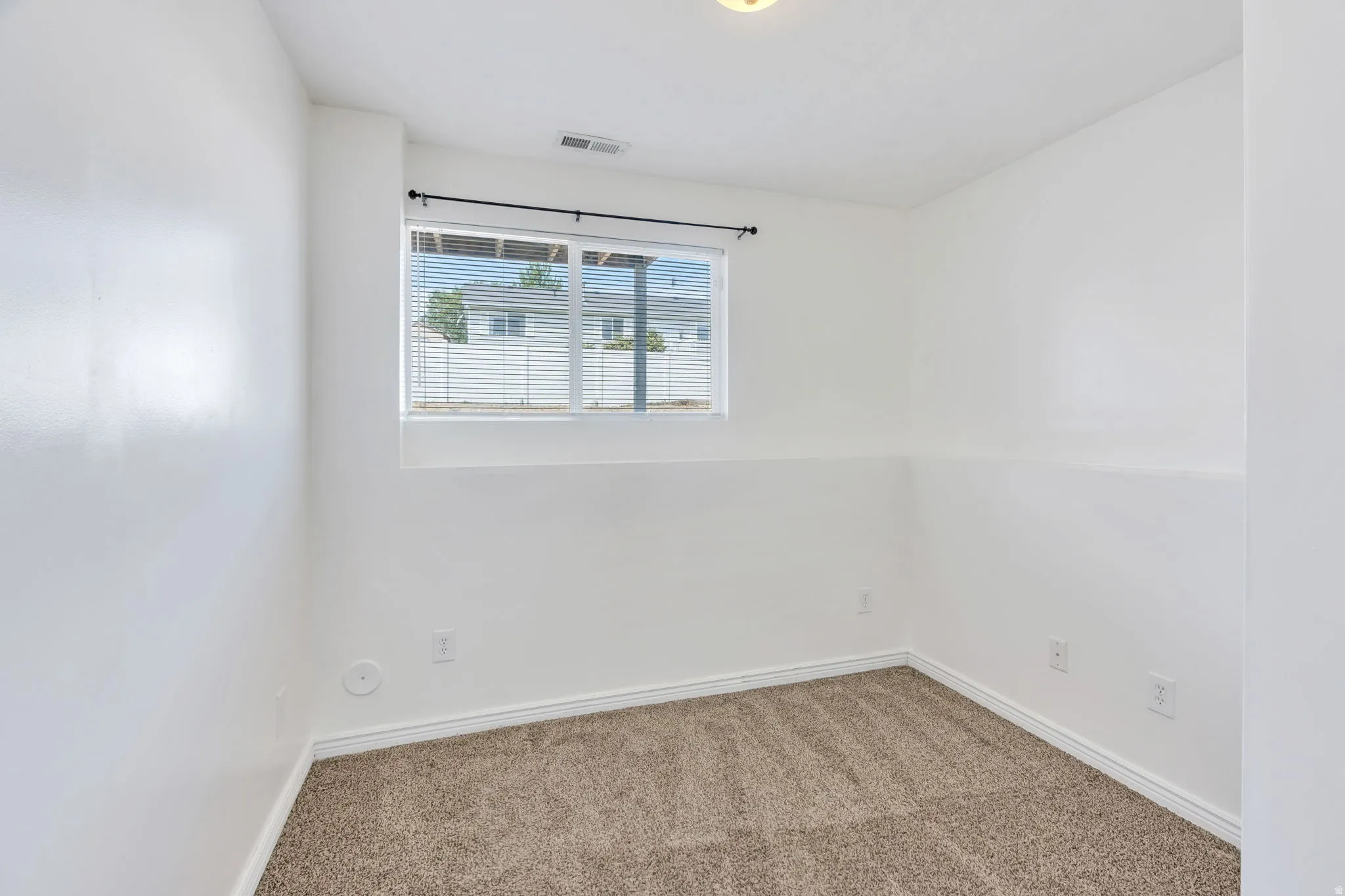 Bright room featuring a window with horizontal blinds, neutral-toned carpet, white walls, and white trim