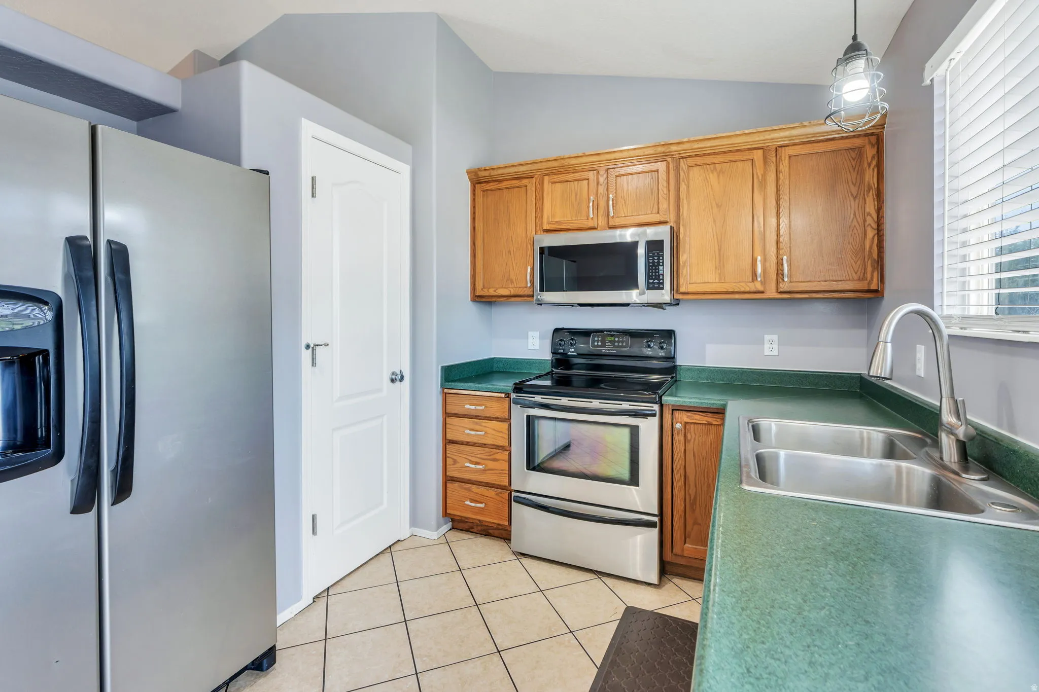 Kitchen featuring stainless steel appliances, wood cabinetry, a dual basin sink, and tile flooring